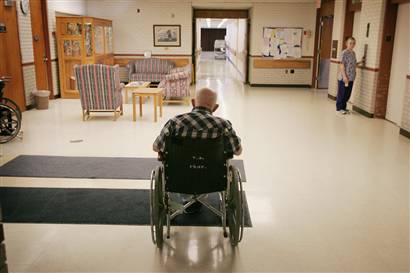 Old man sitting alone in wheelchair in a nursing home facility, viewed from behind