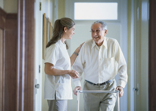 A nurse standing with an elderly nursing home patient with a walker.
