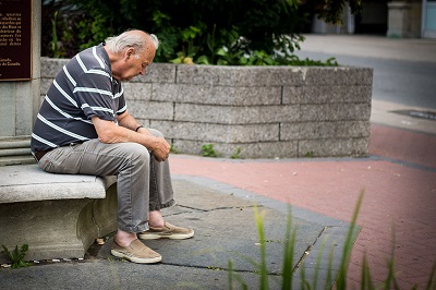 Sad-looking elderly man sitting on a stone bench outside