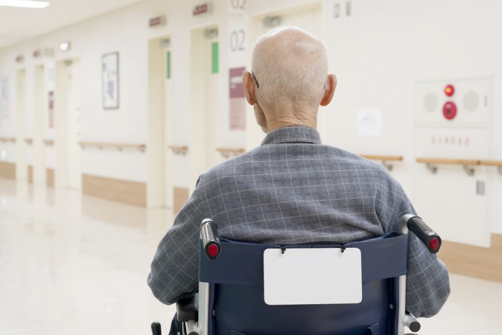 Back view of old man sitting on wheelchair in hospital hallway