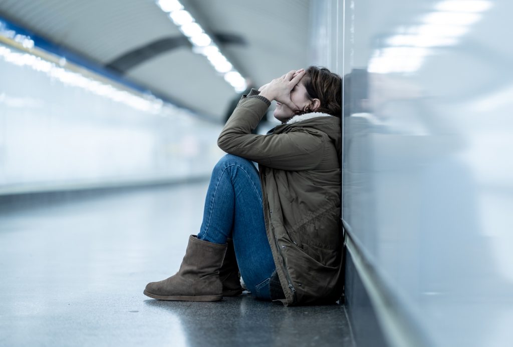 Young adult woman felling shame depressed and hopeless sitting alone in a subway corridor.