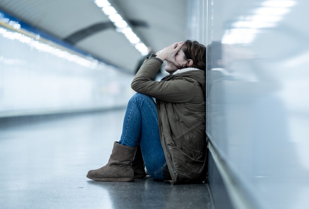 Young adult woman feeling shame depressed and hopeless sitting alone in a subway corridor.