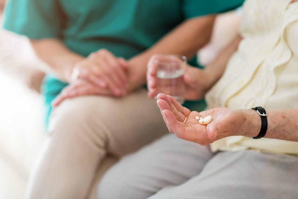 Picture of an elderly patient's hands holding pills and a glass of water sitting next to a nurse