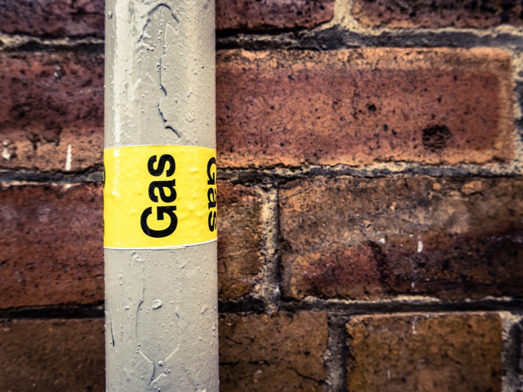 Detail Of A Residential Gas Pipe Against A Red Brick Wall with a yellow label marked "GAS"