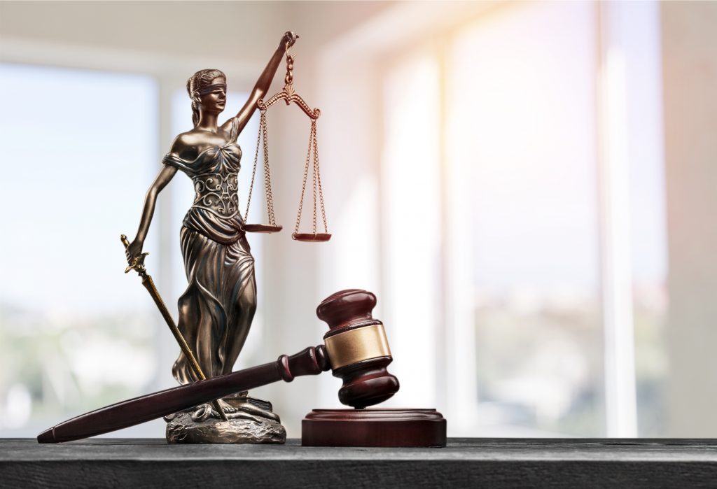 A statue of lady Justice with scales and a sword behind a gavel in a courtroom