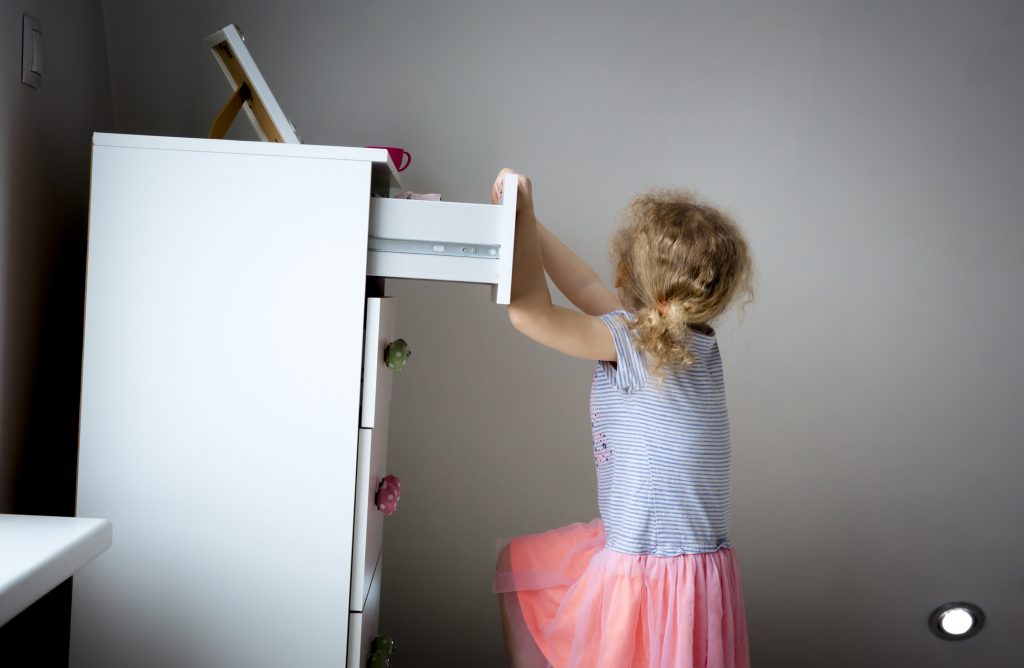 Young girl pulling on the top drawer of a dresser and tipping it over