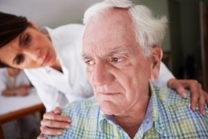 A nurse has her hands on an Elderly man's shoulders and is looking at him. 