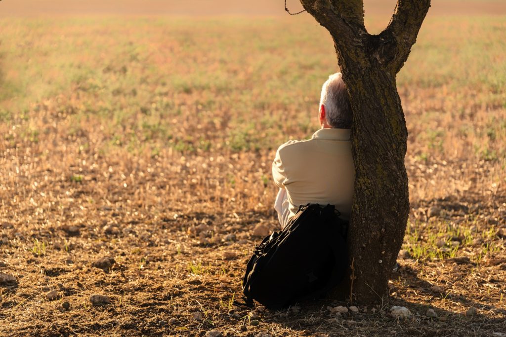 older man resting with his backpack in the shade of a tree