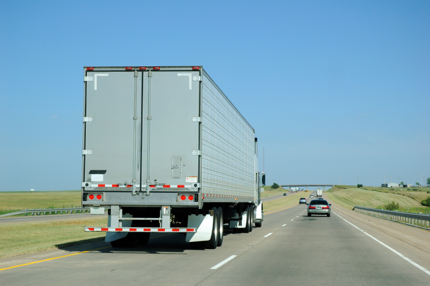 A picture taken from a car driving down a highway passing a semi-truck