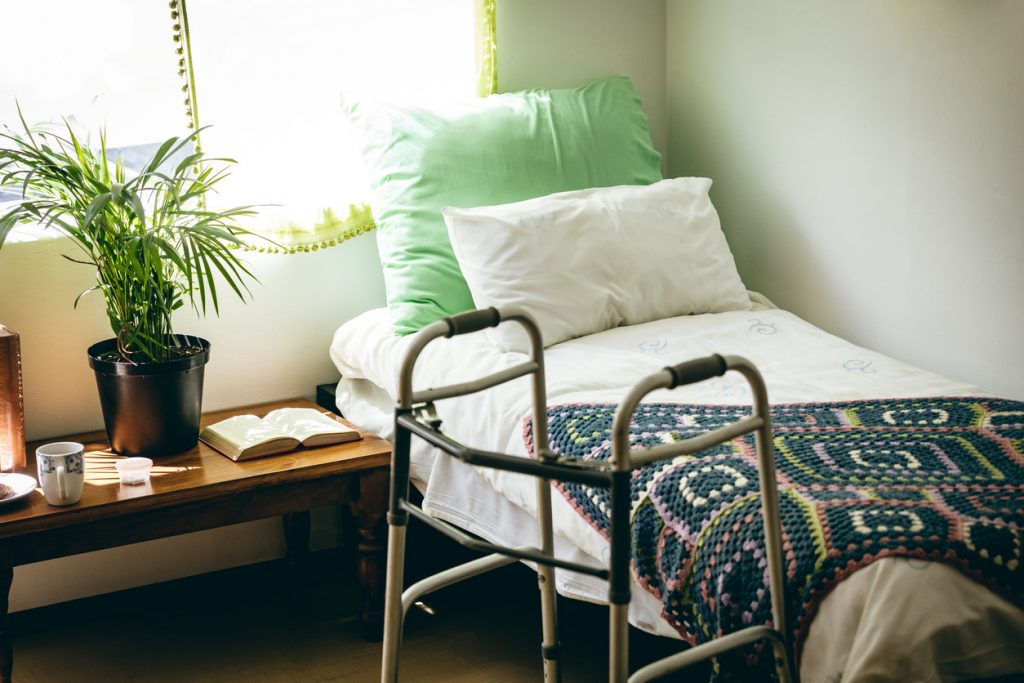 image of  a nursing home bed with a walker beside it. 