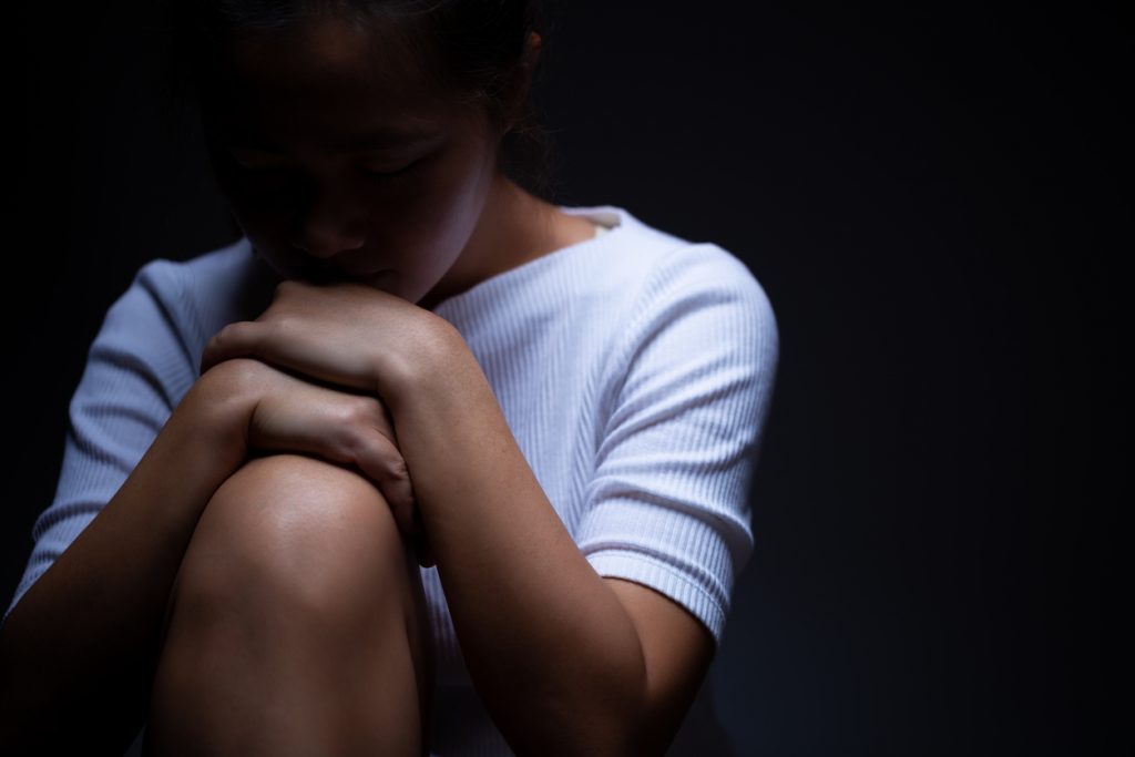 Sad-looking woman sitting in the dark with her hands and chin on her knee