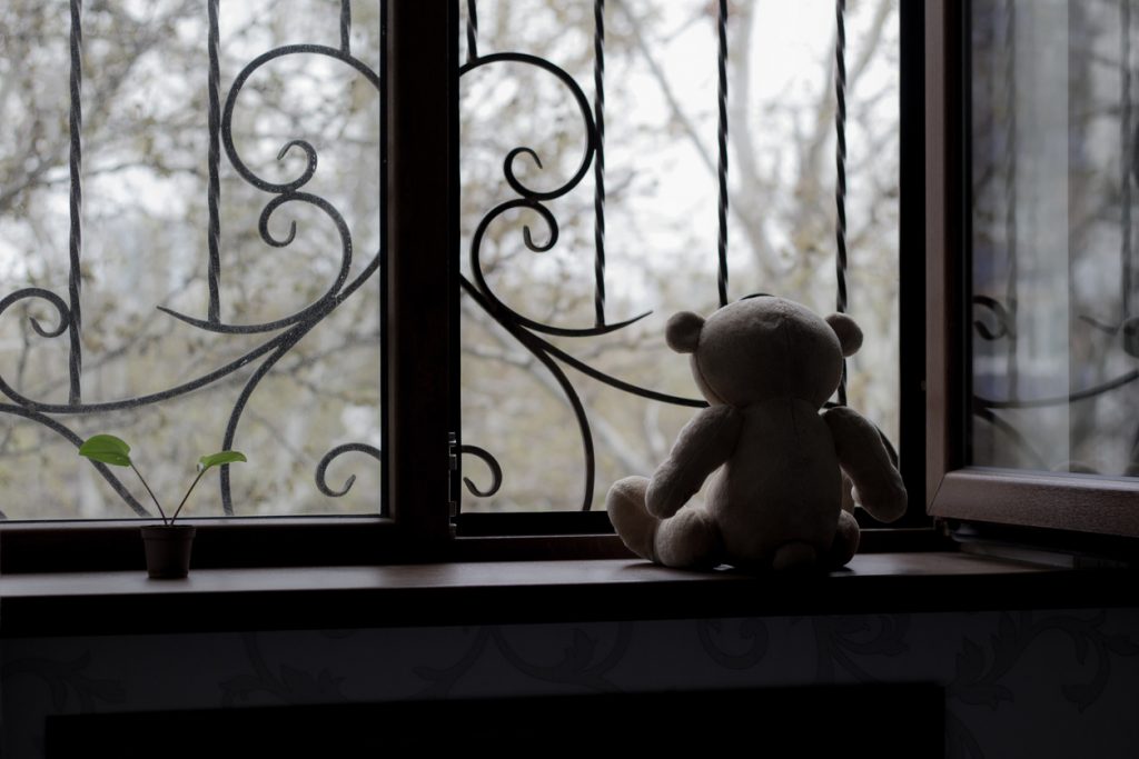 Child's teddy bear sitting on windowsill in a dark room