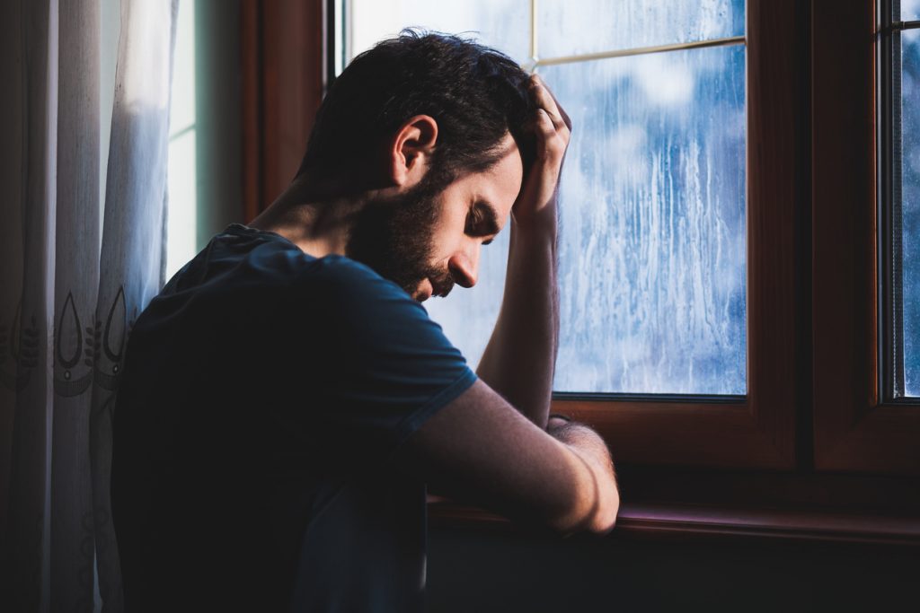 Sad young man sitting by the window