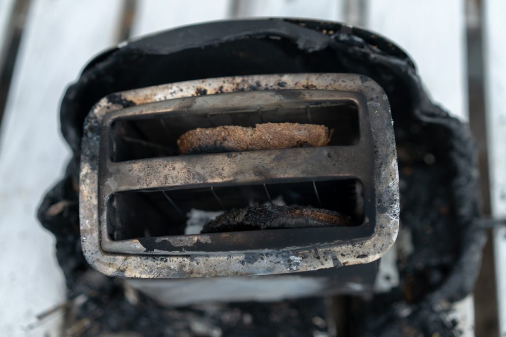 Burnt toaster with two slices of toast caught on fire over white background.