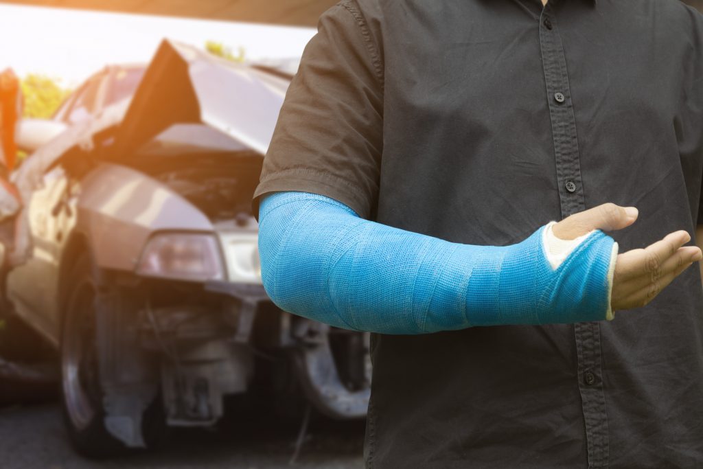 Man wearing an arm cast in front of a car wreck