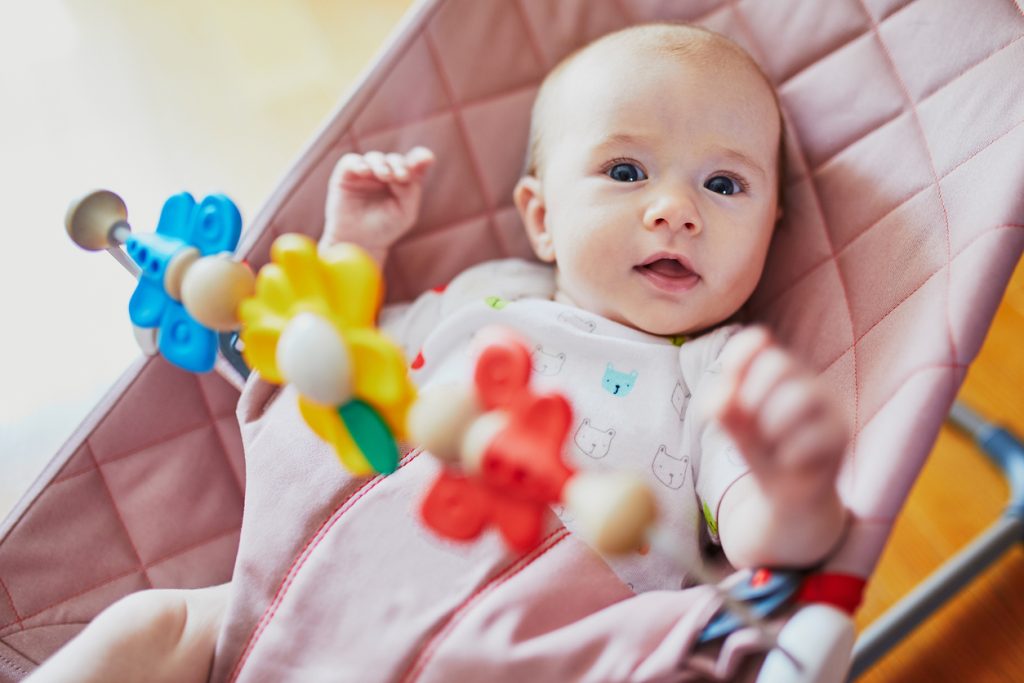 Baby girl sitting in bouncer and playing with colorful toys