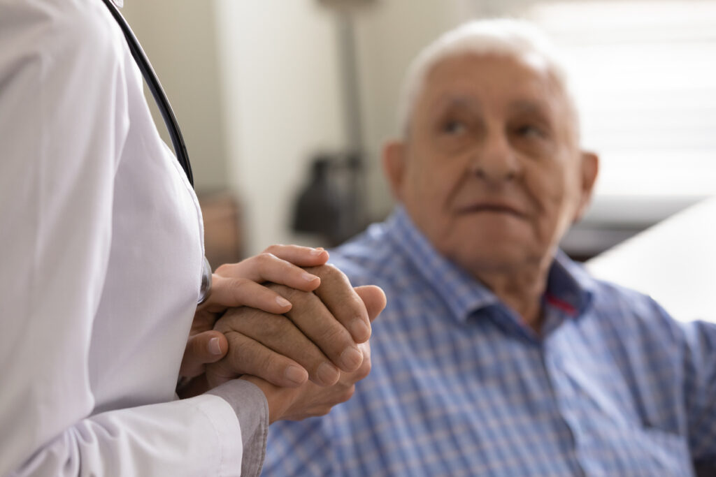 A doctor holding an elderly man's hand in a nursing home