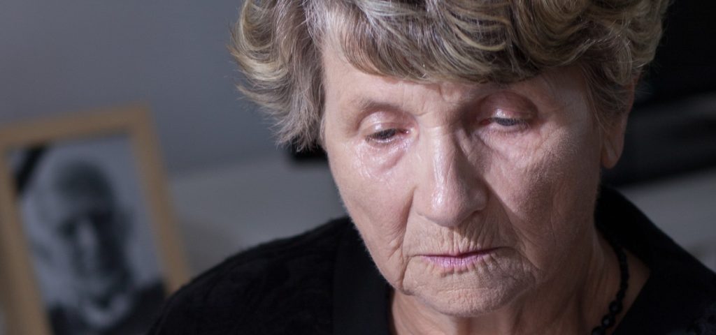 Sad elder woman with a framed picture of a man in the background