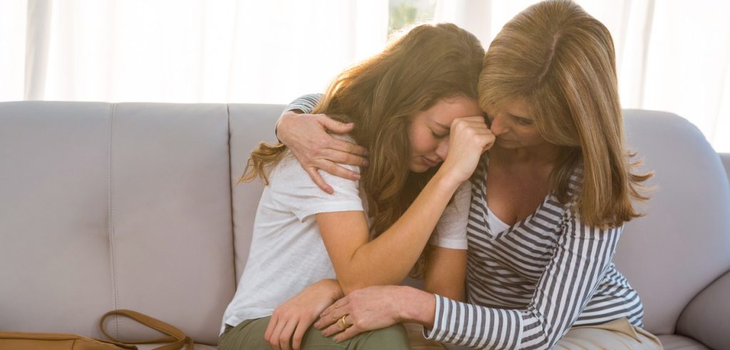 Mother hugging and comforting distressed daughter on the couch