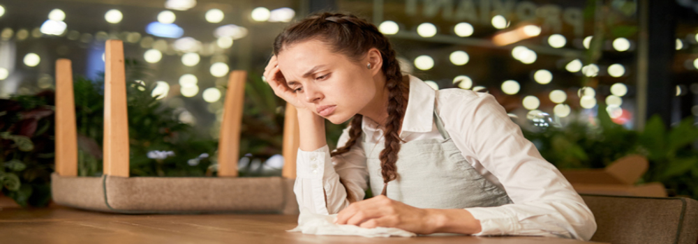 Young worried girl sitting at a restaurant table holding a tissue. 