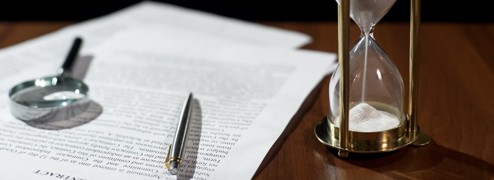 Hour glass sitting next to legal sexual abuse papers with a pen and magnifier on top. 
